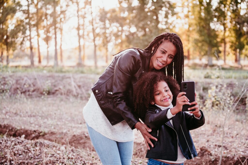 hispanic mother and cute afro kid girl taking selfie at sunset